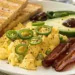 A breakfast plate with eggs, toast, avocado, and jalapeño bacon